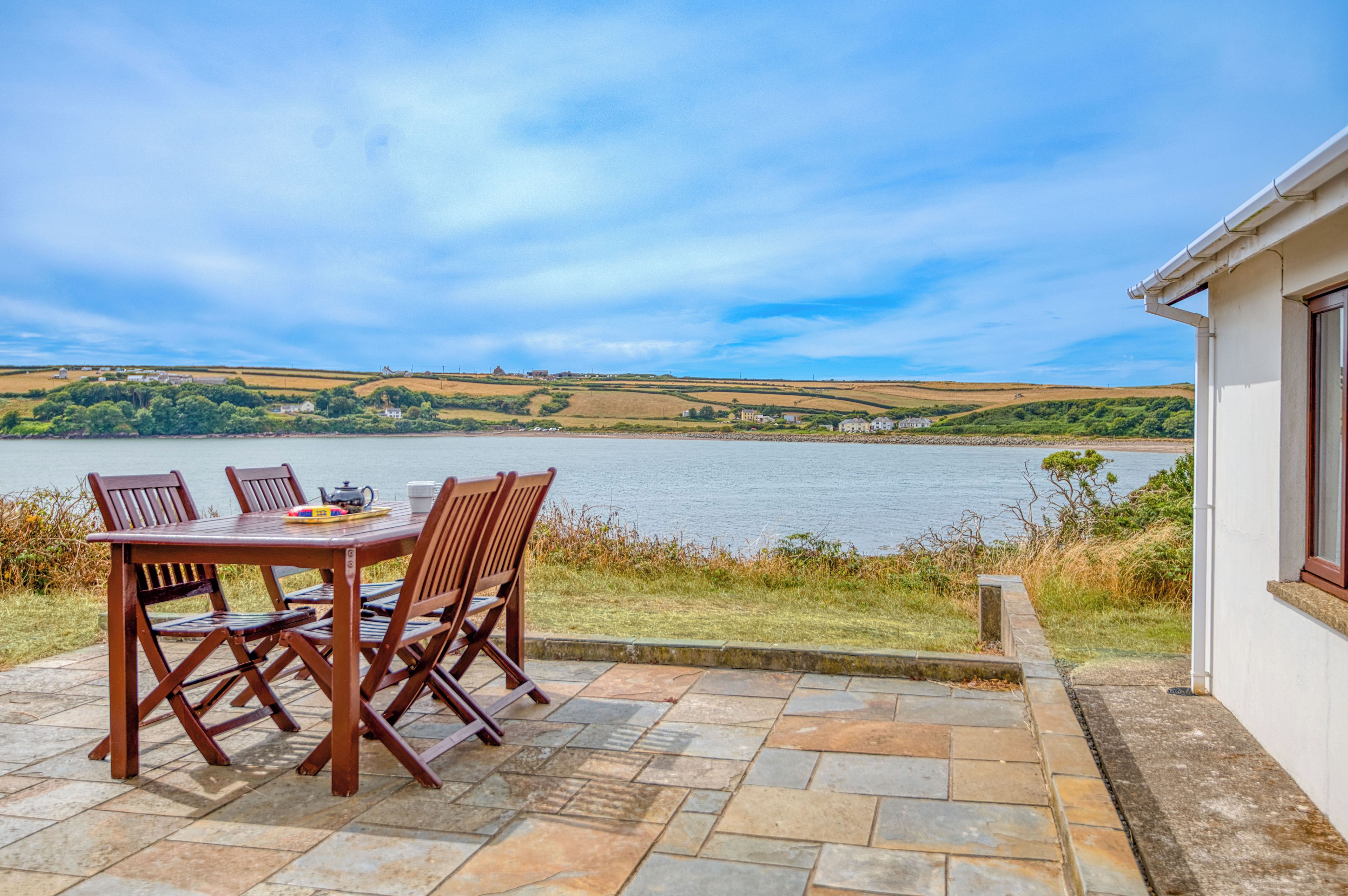 Een terras met tafel en stoelen met uitzicht op een meer, met een vergezicht van heuvels en een heldere lucht.