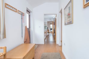 A hallway with wooden flooring, a bench, a coat rack, and a framed picture on the wall.