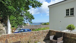 An outdoor patio with wicker furniture, a table set for two, and a view of the sea and buildings in the background. - The Grapes, Holiday Cottage Penally, Sleeps 2, 1 bedrooms,  bathrooms (TENBY)