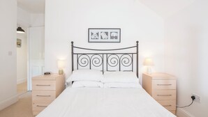 A bedroom with a bed, two bedside tables, a wall-mounted picture, and a door leading to another room. - The Nook, Holiday Cottage Manorbier, Sleeps 4, 2 bedrooms,  bathrooms (Manorbier)