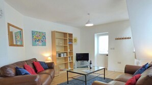 A living room with two brown leather sofas, a glass coffee table, a bookshelf, a flat-screen TV, and a small rug. - The Nook, Holiday Cottage Manorbier, Sleeps 4, 2 bedrooms,  bathrooms (Manorbier)