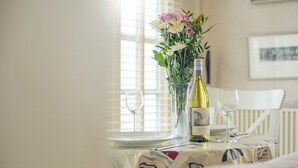 A dining table with a wine bottle, glasses, and a floral arrangement. - The Old Butchers Shop, Holiday Cottage Little Haven, Sleeps 2, 1 bedrooms,  bathrooms (Haverfordwest)
