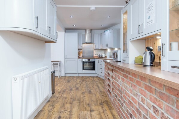 A modern kitchen with white cabinetry, a brick accent wall, a built-in oven, and a coffee machine.