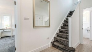 Un escalier dont les marches sont recouvertes de moquette, menant à un palier situé au deuxième étage.