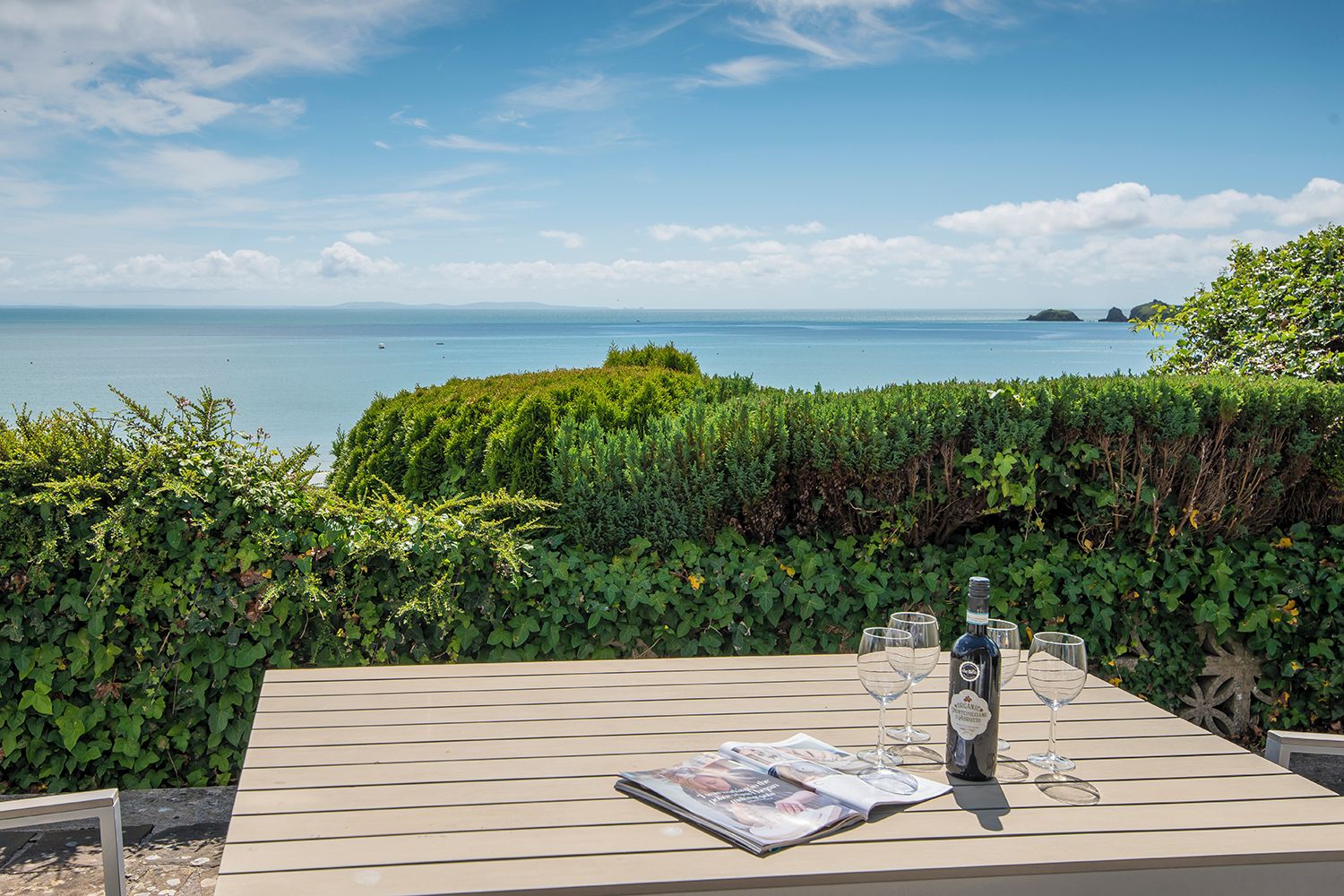 A table set outdoors with a bottle and glasses, overlooking a body of water and greenery.
