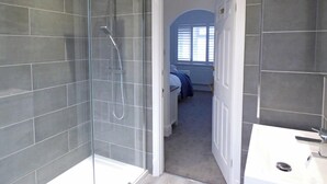 Une salle de bain moderne avec une douche en verre, un lavabo blanc et une chambre visible avec un lit et une fenêtre.