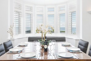 A dining table set for six with white plates, silverware, and wine glasses, flanked by black leather chairs. - The Rath, Holiday Cottage Saundersfoot, Sleeps 6, 3 bedrooms,  bathrooms (SAUNDERSFOOT)
