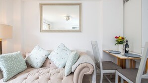 Un salon moderne avec un canapé capitonné, une table à manger avec des chaises, un miroir et un vase rempli de fleurs.