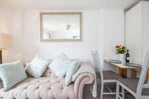 A modern living room with a tufted sofa, a dining table with chairs, a mirror, and a vase with flowers. - The Rath Cottage, Holiday Cottage Saundersfoot, Sleeps 2, 1 bedrooms,  bathrooms (SAUNDERSFOOT)