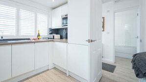 A modern kitchen with white cabinetry, a built-in oven, and a window with blinds. - The Rath Cottage, Holiday Cottage Saundersfoot, Sleeps 2, 1 bedrooms,  bathrooms (SAUNDERSFOOT)