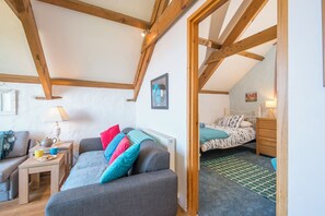 Une chambre à coucher confortable, aménagée dans un grenier avec des poutres apparentes, un lit recouvert d’une literie à motifs, une petite table de chevet et une commode.