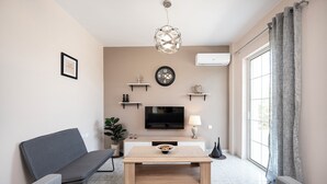 A modern living room with a sofa, a coffee table, a TV, and decorative items on shelves.