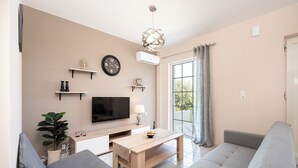 A modern living room with a flat-screen TV, a wooden coffee table, a grey sofa, and a potted plant.