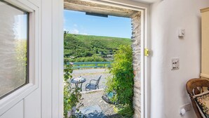 A doorway leading to a patio with a table and chairs, a stone wall, and a view of a green hillside. - The Smithy, Holiday Cottage Abercastle, Sleeps 2, 1 bedrooms,  bathrooms (Haverfordwest)