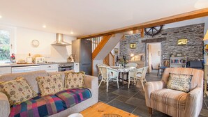A cozy living room with a sofa, armchair, and coffee table. A dining area with a table and chairs is visible in the background. - The Smithy, Holiday Cottage Abercastle, Sleeps 2, 1 bedrooms,  bathrooms (Haverfordwest)