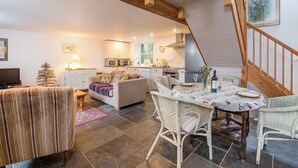 A cozy living room with a sofa, a dining table set for two, and a kitchen in the background. - The Smithy, Holiday Cottage Abercastle, Sleeps 2, 1 bedrooms,  bathrooms (Haverfordwest)