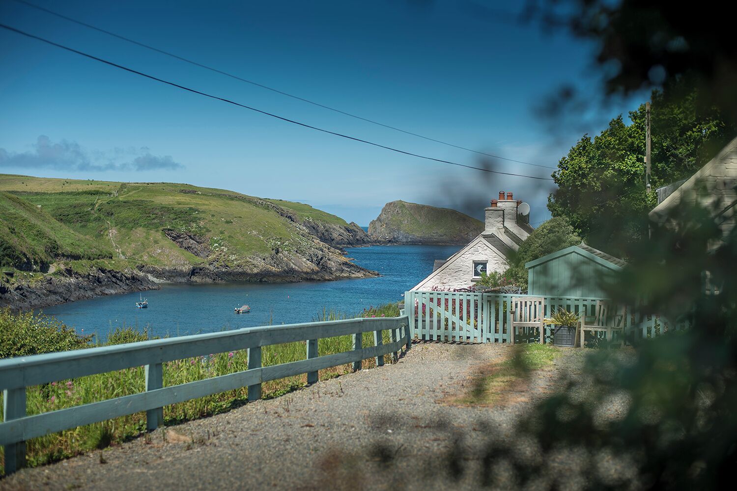 A coastal view with a stone building, a wooden fence, and a clear blue sea.