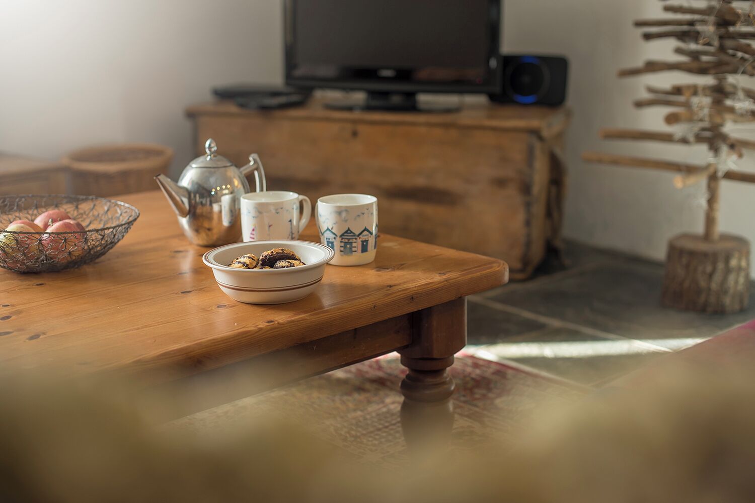 Een houten tafel met een schaal koekjes en een theepot.