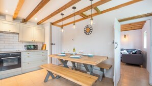 A kitchen with wooden beams, a dining table with benches, and a clock on the wall. - The Stables and Bullpen, Holiday Cottage Castlemartin, Sleeps 6, 3 bedrooms,  bathrooms (Pembroke)