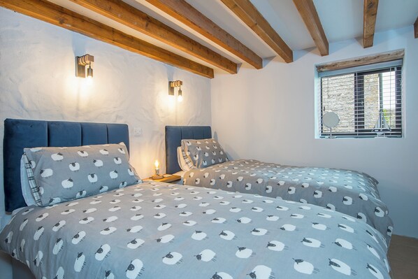 A bedroom with two beds, wooden beams, and a window with blinds.