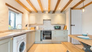 A compact kitchen with a washing machine, oven, and wooden beams on the ceiling. - The Stables and Bullpen, Holiday Cottage Castlemartin, Sleeps 6, 3 bedrooms,  bathrooms (Pembroke)