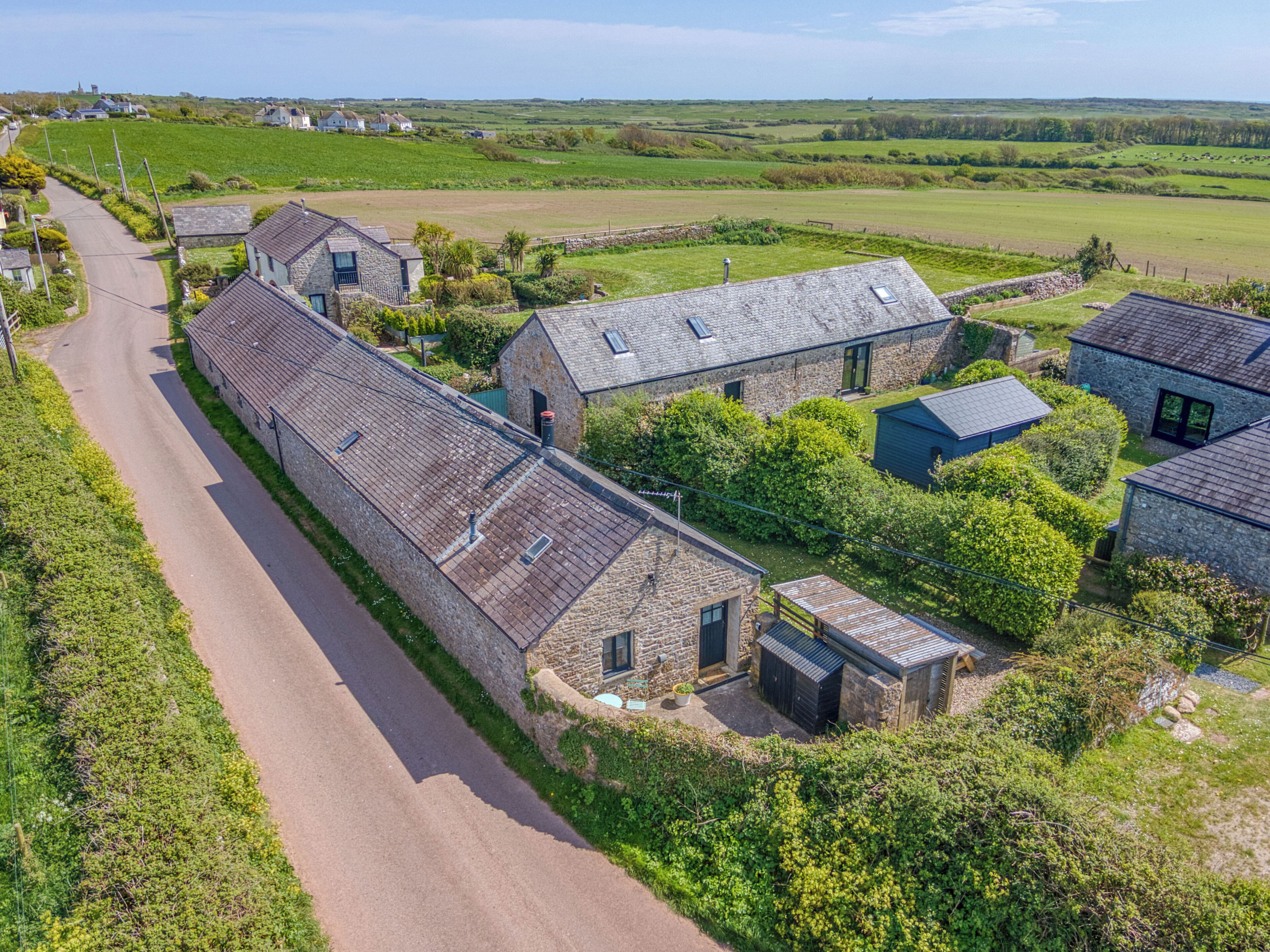 A rural property with stone buildings, a paved road, and surrounding fields.