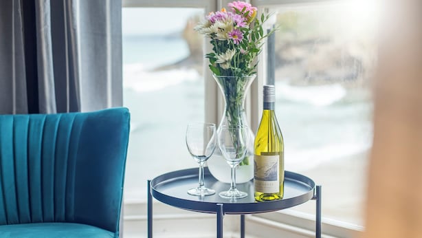 Een kamer met een blauwgroene bank, een kleine ronde tafel met een fles wijn, twee glazen en een vaas met bloemen.