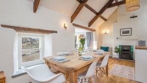 Een eetgedeelte met een houten tafel voor vier personen, witte stoelen en een uitzicht door een raam.