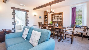 A cozy living room with a blue sofa, a dining area with wooden chairs and a table, and a stone wall. - Tides Reach, Holiday Cottage Cwm yr Eglwys, Sleeps 6, 3 bedrooms,  bathrooms (Newport)