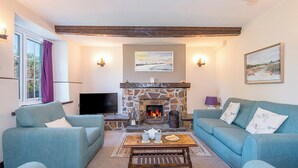 A cozy living room with a stone fireplace, two blue sofas, a coffee table, and a television. - Tides Reach, Holiday Cottage Cwm yr Eglwys, Sleeps 6, 3 bedrooms,  bathrooms (Newport)