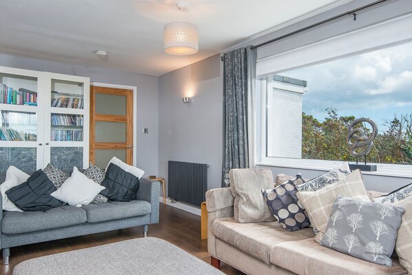 A modern living room with two sofas, a bookshelf, and a large window with a view.