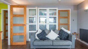 A modern living room with a grey sofa, wooden doors, and a bookshelf filled with books.