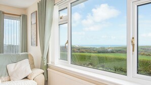 A room with a view of a green landscape through large windows, a sofa with a throw blanket, and a radiator. - Trefisheg Bungalow, Holiday home Strumble Head, Sleeps 6, 3 bedrooms,  bathrooms (Strumble Head)