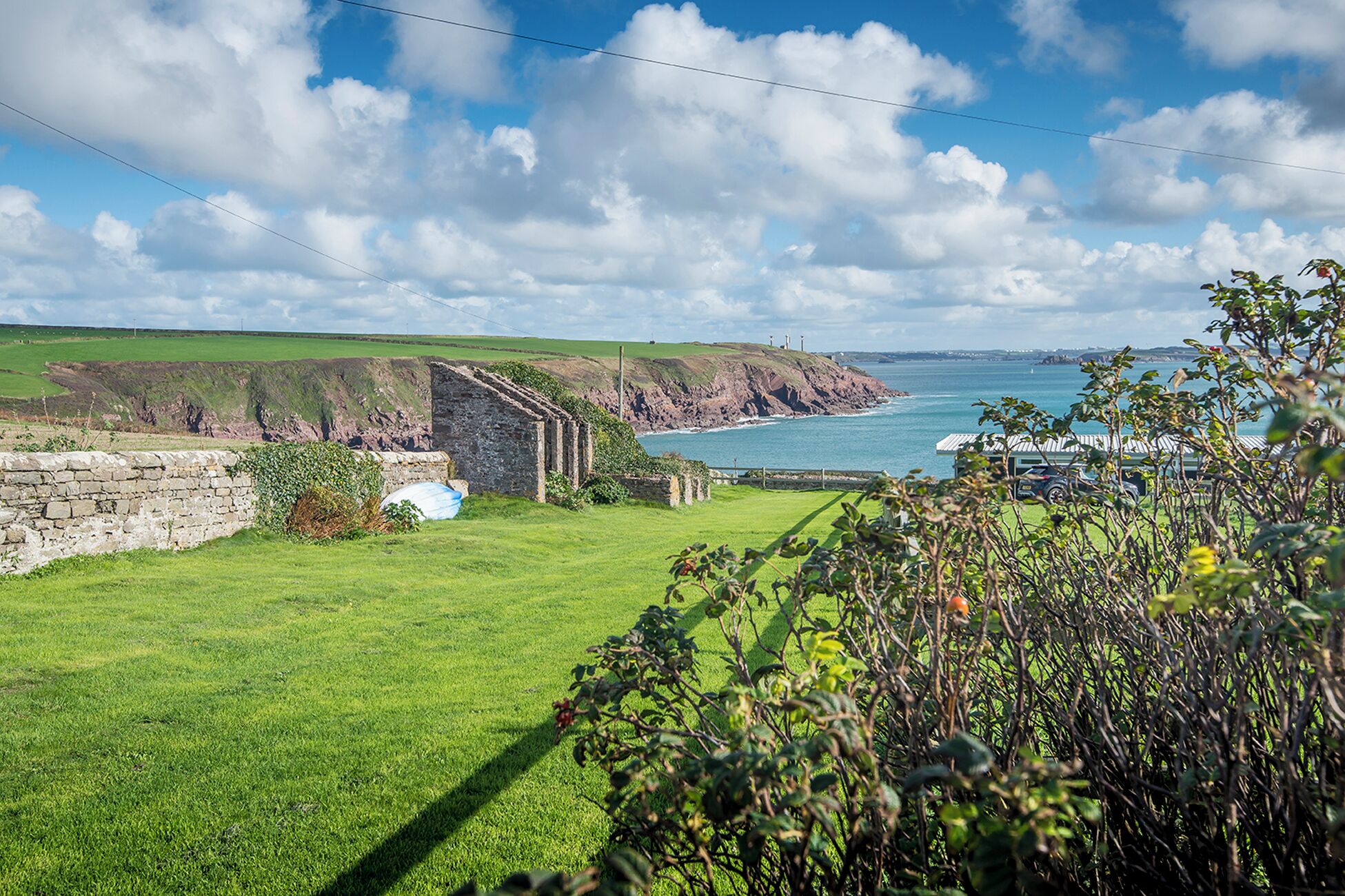 A coastal landscape with a grassy field, stone walls, and a small building.