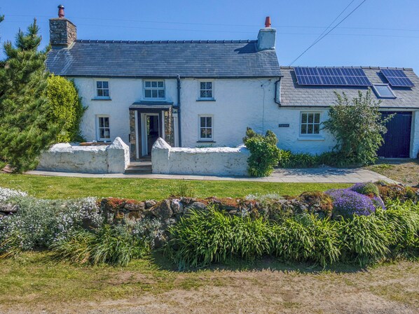 Une maison à deux étages avec une façade en pierre, une porte d’entrée et des panneaux solaires sur le toit.