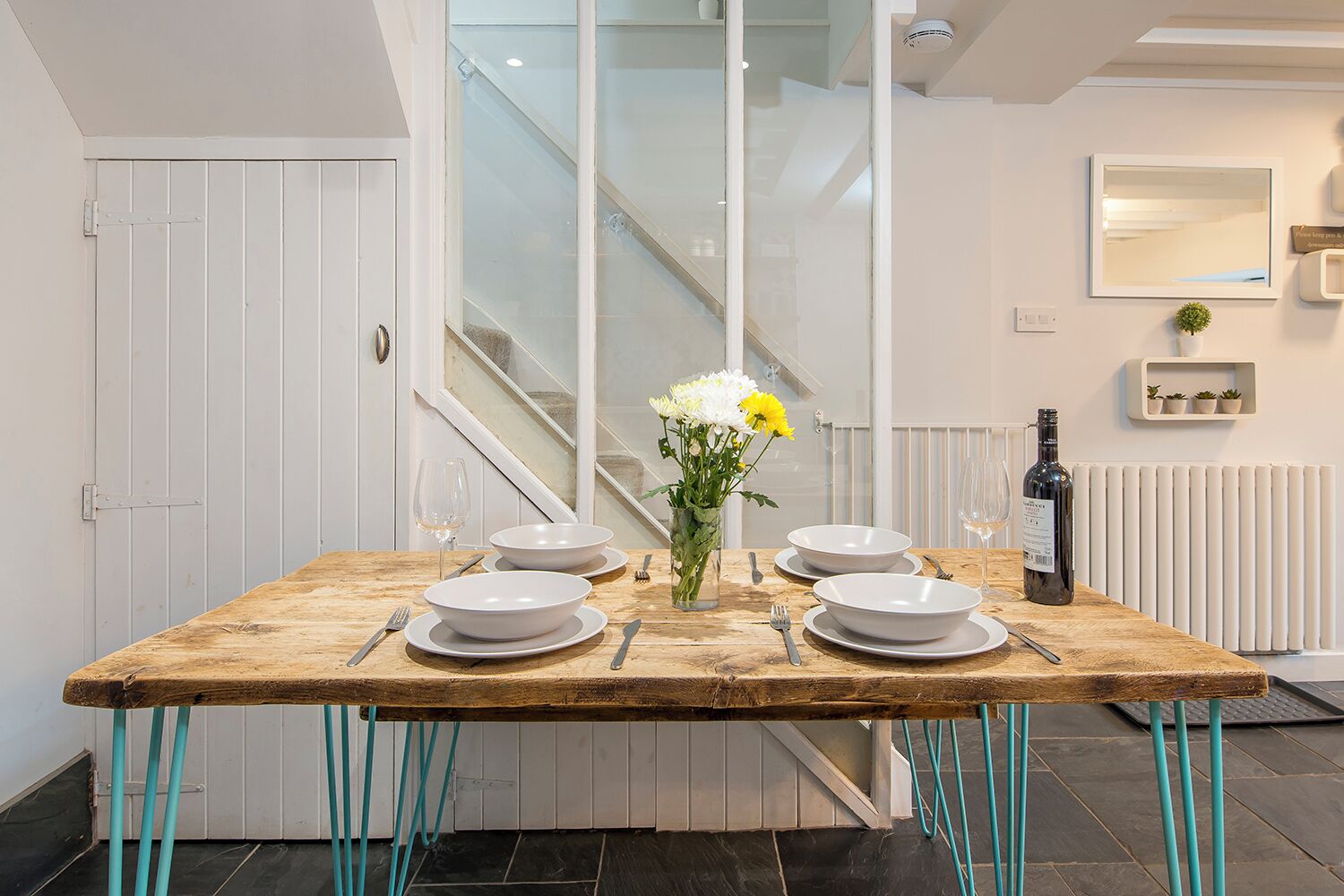 A dining table set with white plates, bowls, and cutlery, a vase with flowers, and a bottle of wine.