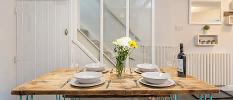 A dining table set with white plates, bowls, and cutlery, a vase with flowers, and a bottle of wine.