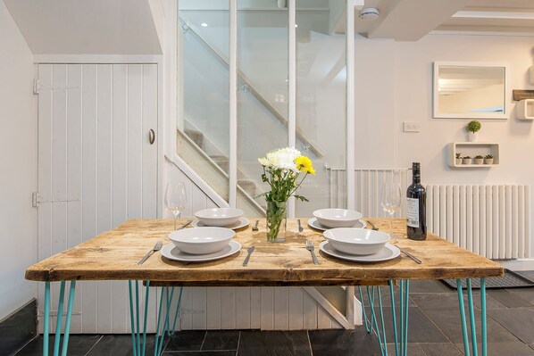 A dining table set with white plates, bowls, and cutlery, a vase with flowers, and a bottle of wine.