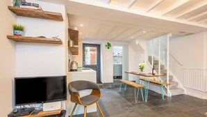 Un salon moderne avec un téléviseur, des étagères en bois, un fauteuil, une table à manger avec des bancs et un escalier.