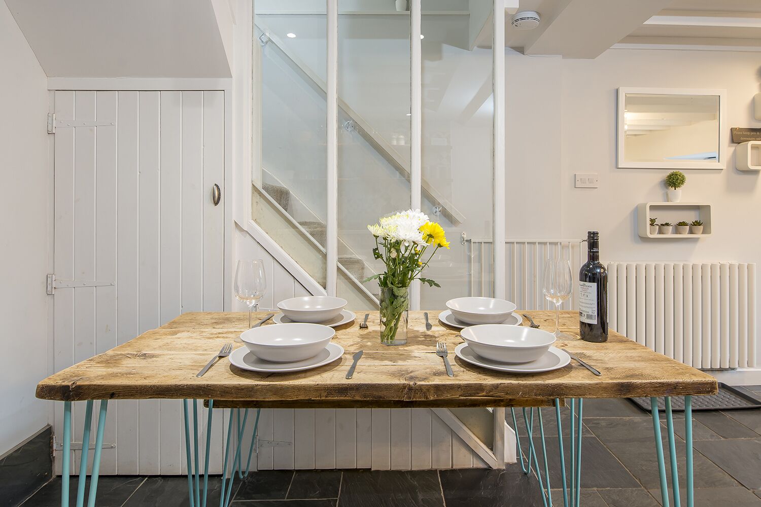 A dining table set with white plates, bowls, and cutlery, a vase with flowers, and a bottle of wine.