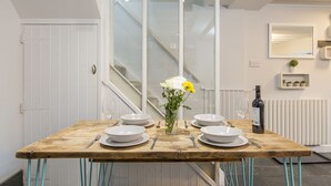 Une table à manger dressée avec de l’assiette, des bols et des couverts blancs, un vase rempli de fleurs et une bouteille de vin.