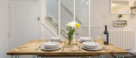 A dining table set with white plates, bowls, and cutlery, a vase with flowers, and a bottle of wine.