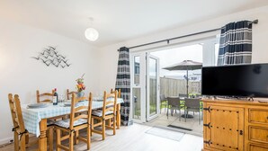 Ein Essbereich mit einem Tisch für vier Personen, Holzstühlen, einem Fernseher auf einem Holzschrank und einer Glasschiebetür, die auf eine Außenpatio führt.