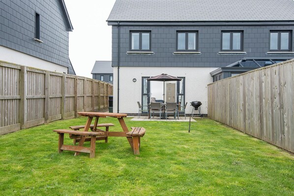 A backyard with a picnic table, a barbecue grill, and a covered patio area.