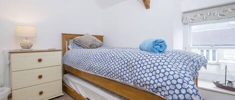 Een slaapkamer met een bed, een dressoir, een lamp, een raam met uitzicht op een dorp, en een ingelijst schilderij aan de muur.