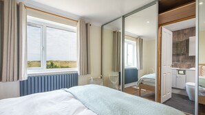 Ein Schlafzimmer mit einem großen Bett, Blick ins Freie durch ein Fenster, ein Badezimmer mit Dusche und Toilette sowie ein Spiegel, der den Raum reflektiert.