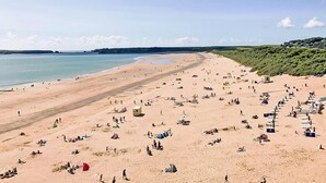 Ein weiter Sandstrand mit Menschen und Zelten, ein klarer Himmel und ferne Klippen.