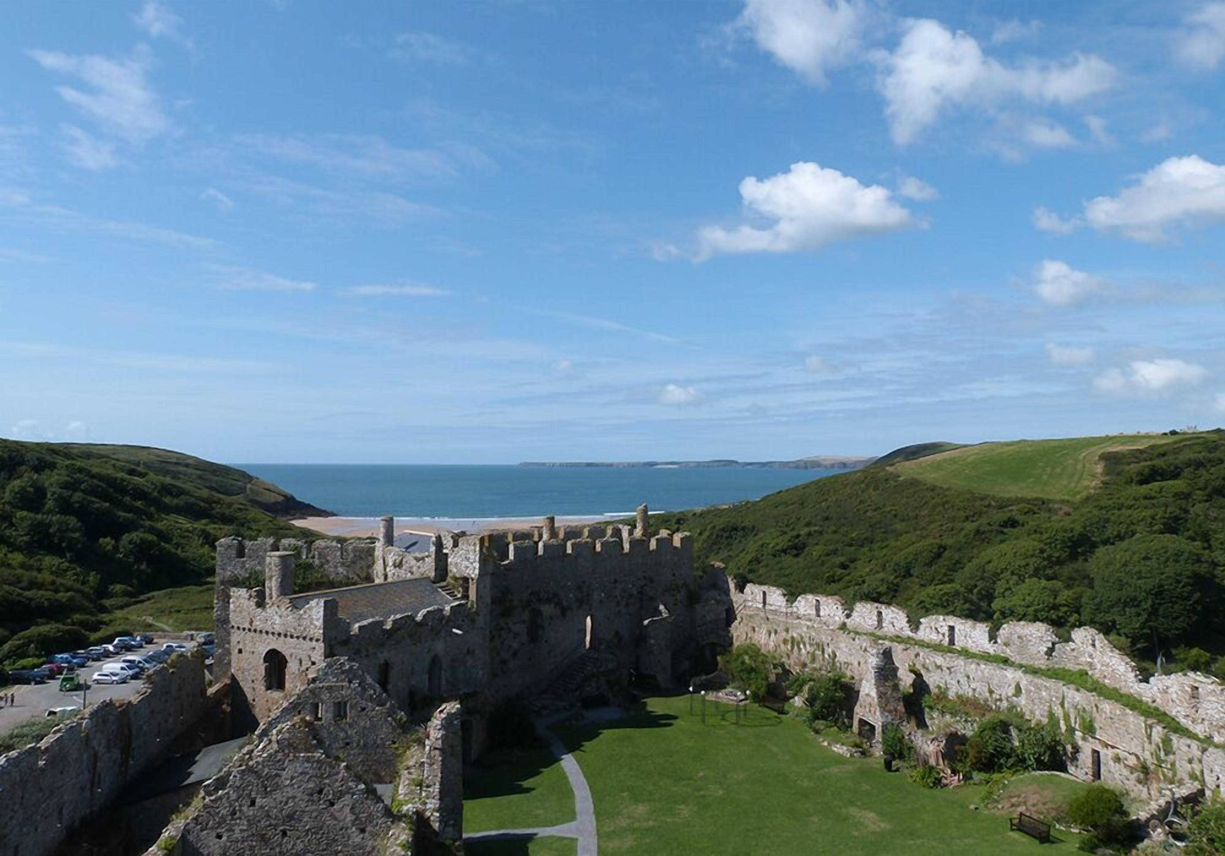 A historic castle with a fortified wall, a grassy courtyard, and a view of the sea.