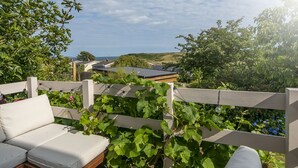 Eine Terrasse mit einer weißen, gepolsterten Couch, einem Holzzaun und Blick auf das Meer und die Hügel.