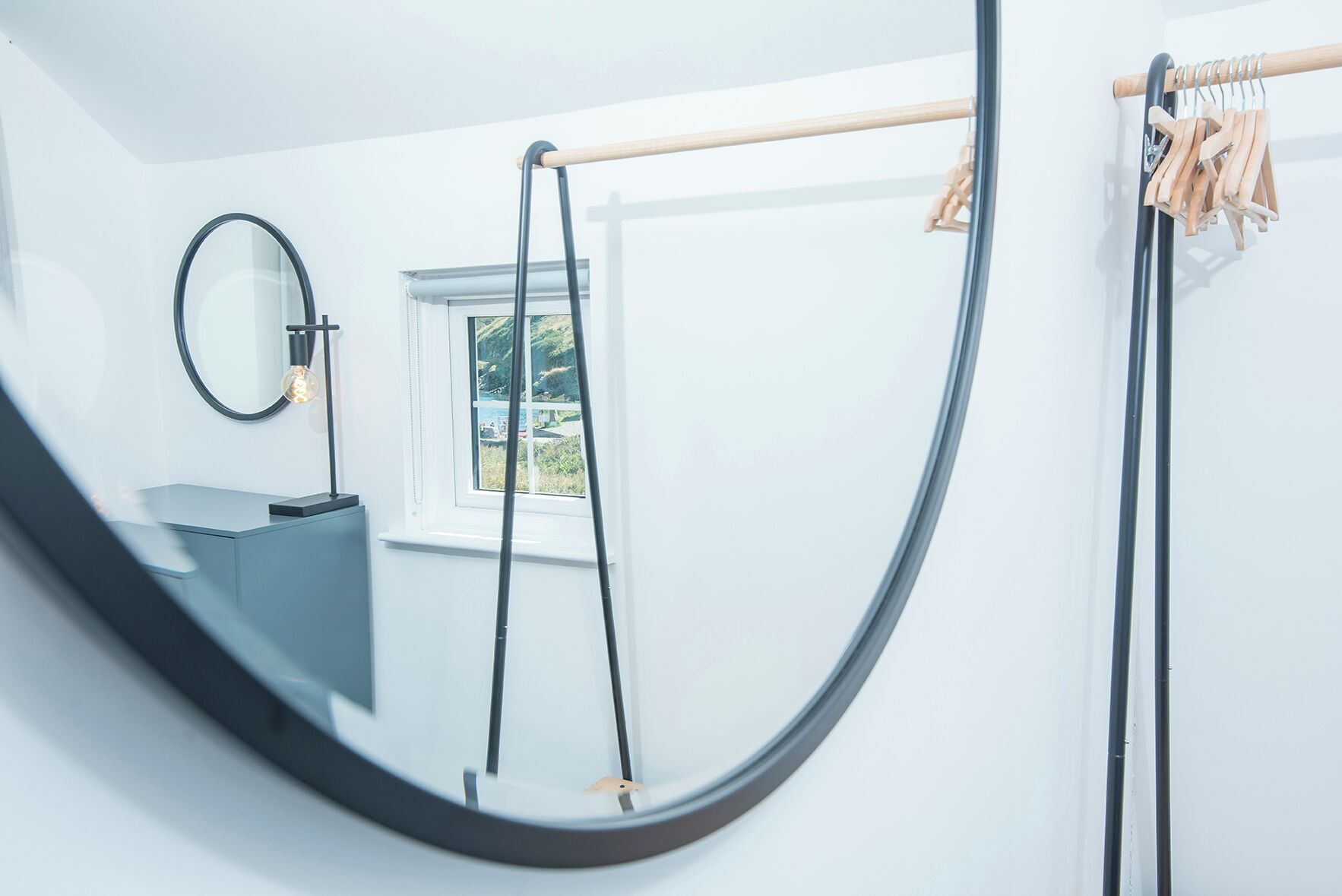 A modern bathroom with a round mirror, a sink, and a window with a view of greenery.
